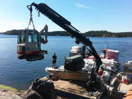 Kranpråmen Robert fraktar ut byggmaterial och en liten grävmaskin till Viggsö.